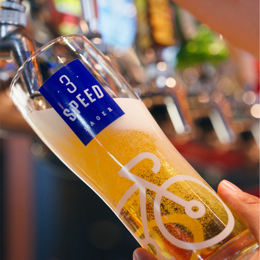 Glass of 3 Speed Lager being tapped at Amsterdam Brewhouse, featuring a lakeside view and rooftop ambiance